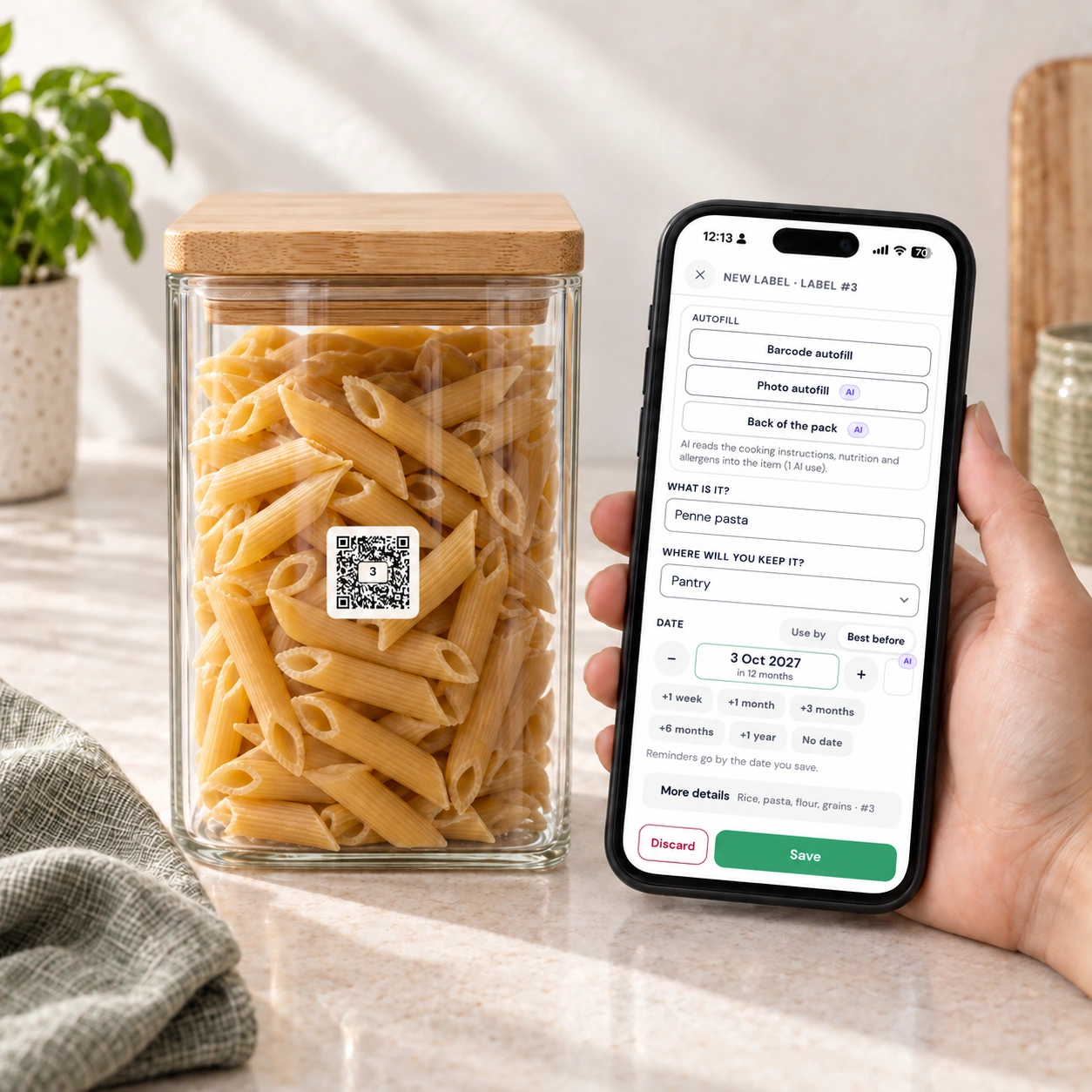 A phone beside a labelled jar of penne, showing the QR Pantry entry form with the name, pantry location, best-before date and Save button
